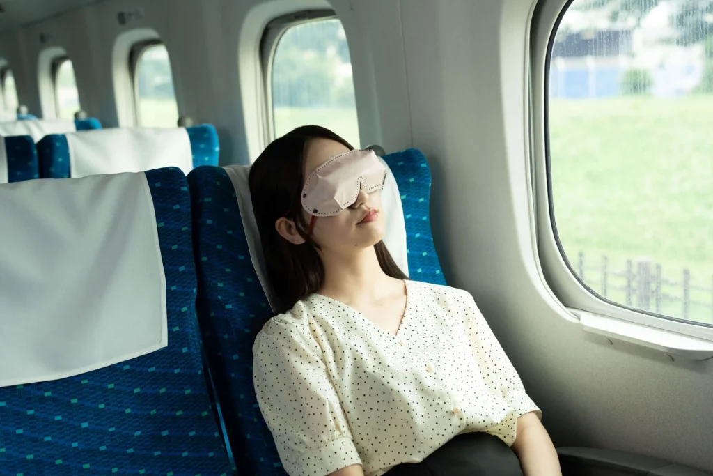 アイマスクを付けて新幹線で仮眠を取る女性